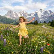 Young girl in yellow dress running through a wildflower meadow with snow-covered mountains in the background